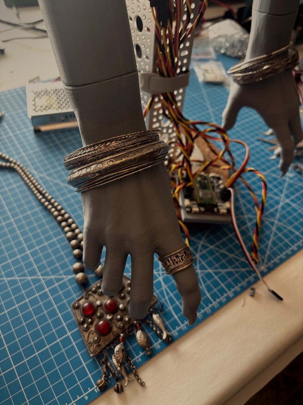 Lupa's grey clawed hand in stacked silver bangles and rings, beside a jeweled pendant on the bench