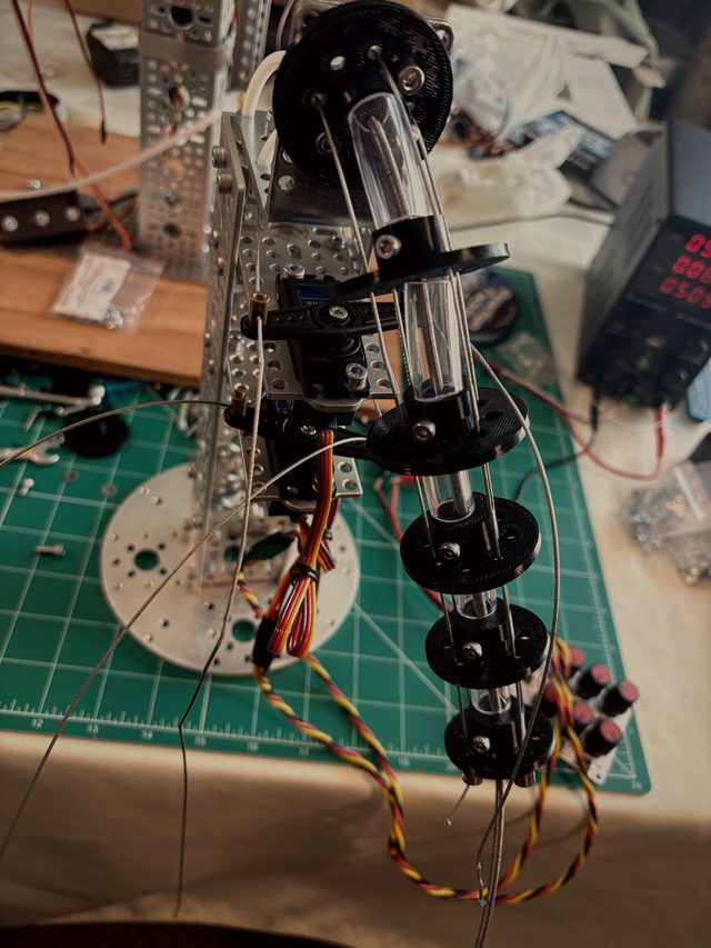 Tail test rig: black discs stacked on a clear tube beside the aluminum frame, servo leads trailing