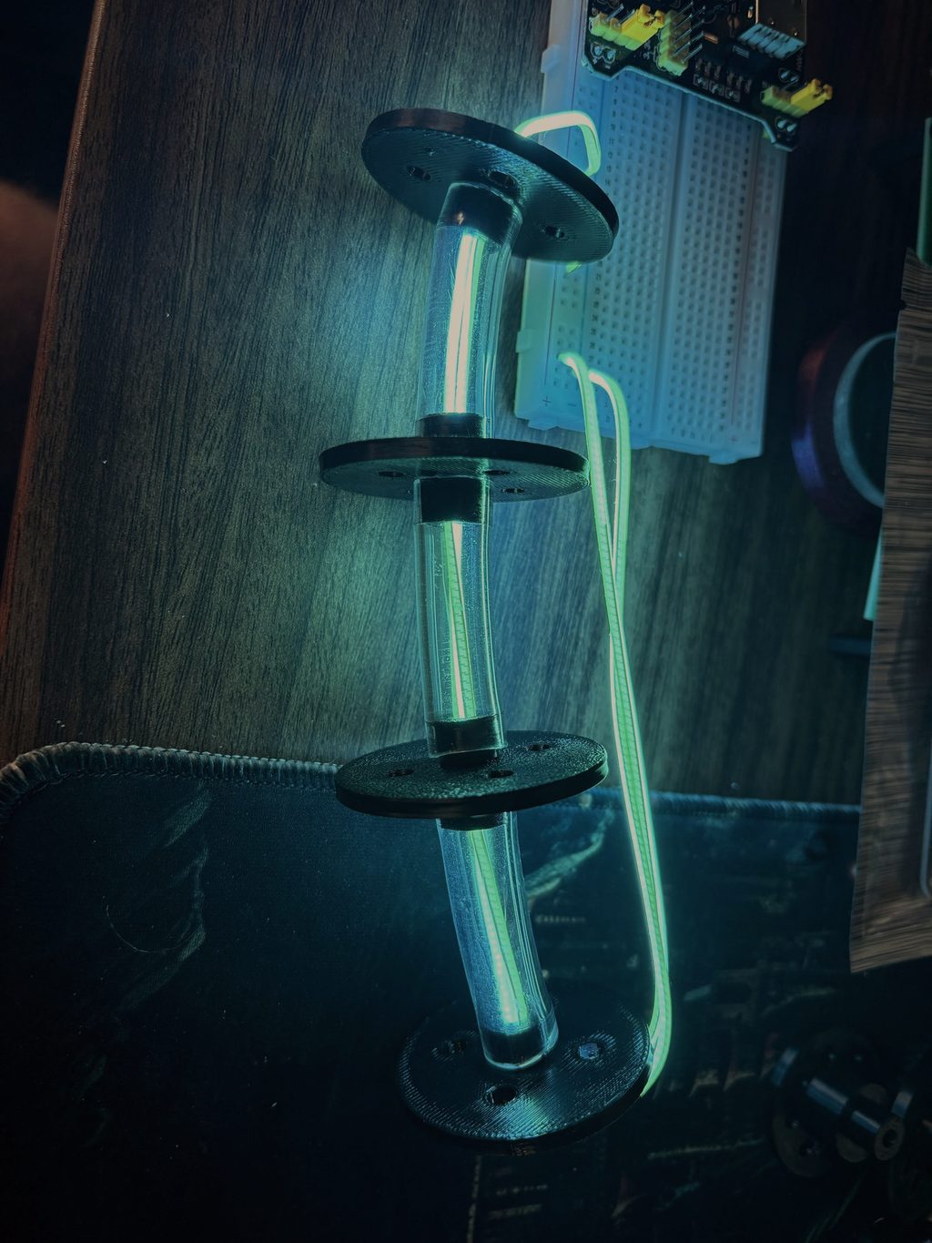 A glowing cyan light tube threaded through black servo discs, lit in the dark