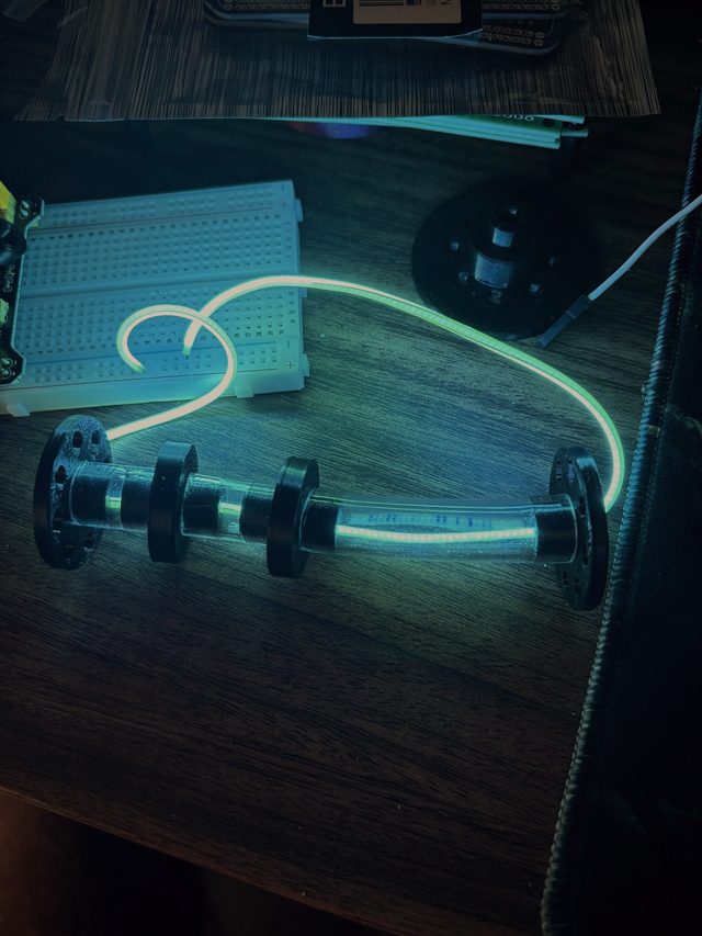 The glowing light tube curving across the bench beside a breadboard