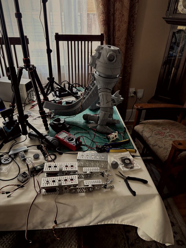 Workbench overview: headless MechaGodzilla lower body and tail on a cutting mat with tools