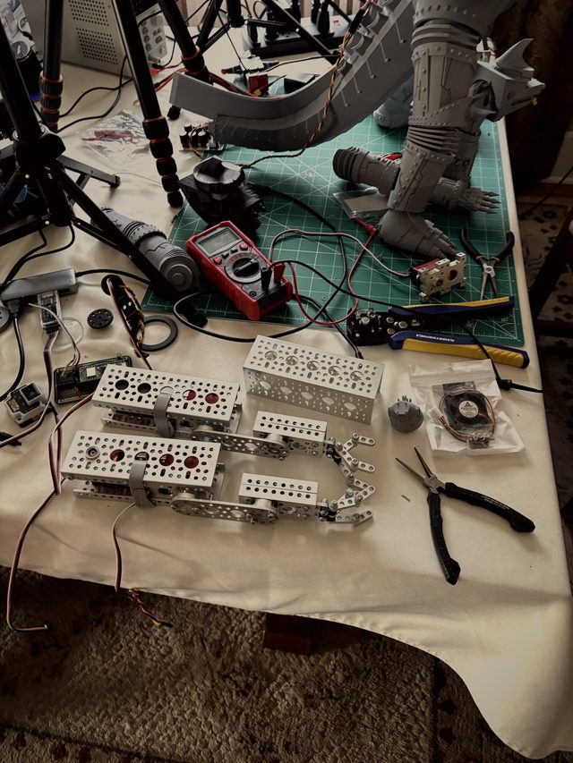 Disassembled parts on the bench: tail section, leg, and servo-mounted aluminum brackets