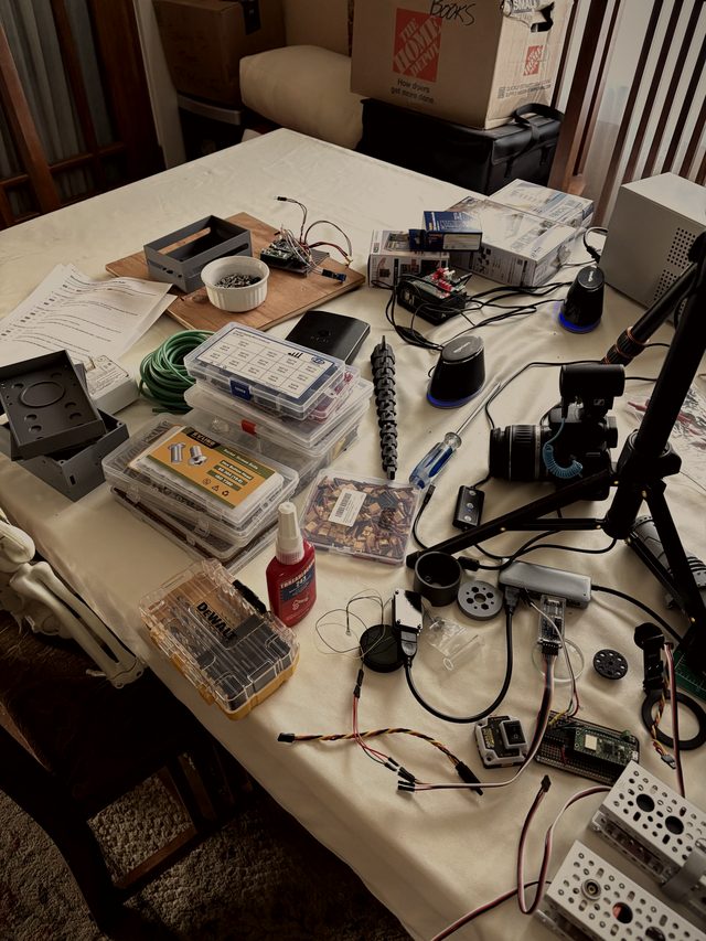 Workbench covered in build supplies: parts organizers, threadlocker, drill bits, and servo extension wires