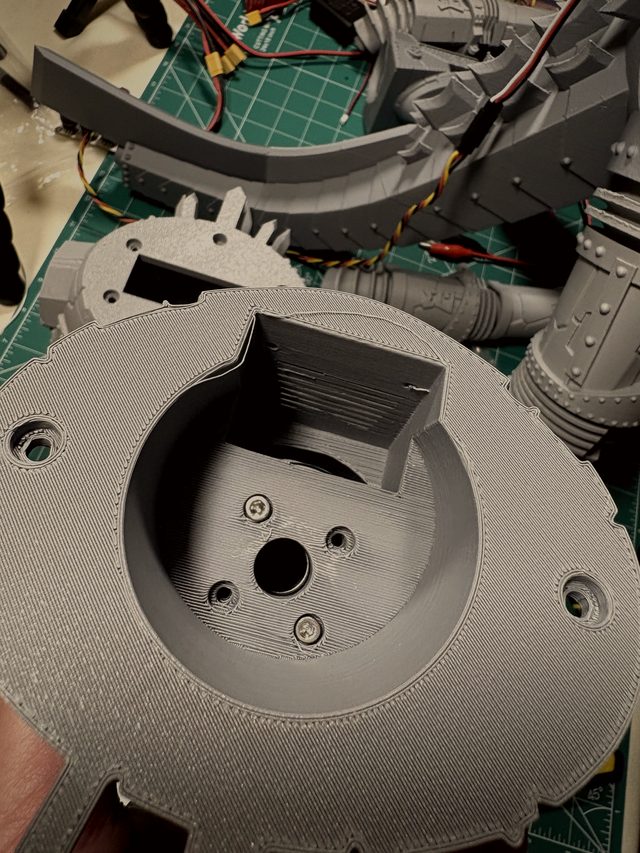 3D-printed base plate with screwed-in servo mount held in hand, tail assembly behind