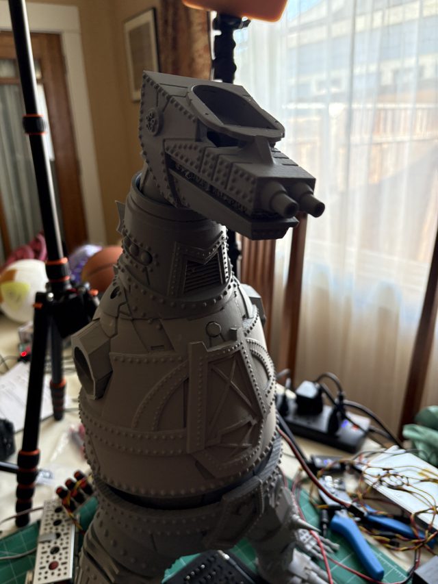 Unpainted gray 3D-printed MechaGodzilla head and riveted torso, three-quarter view on a workbench