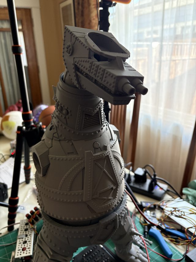MechaGodzilla head and riveted torso by a window, wiring and tools on the workbench below