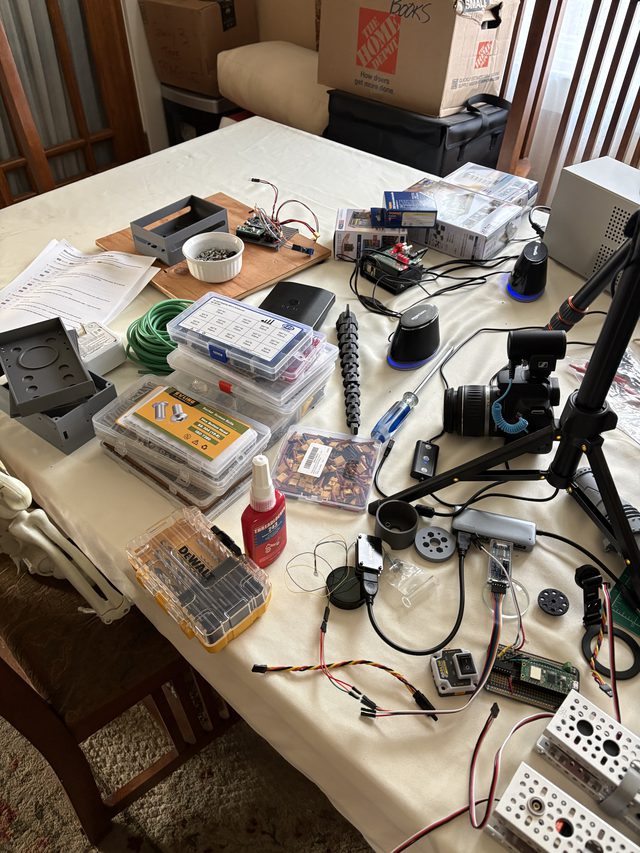 Workbench covered in build supplies: parts organizers, threadlocker, drill bits, and servo extension wires