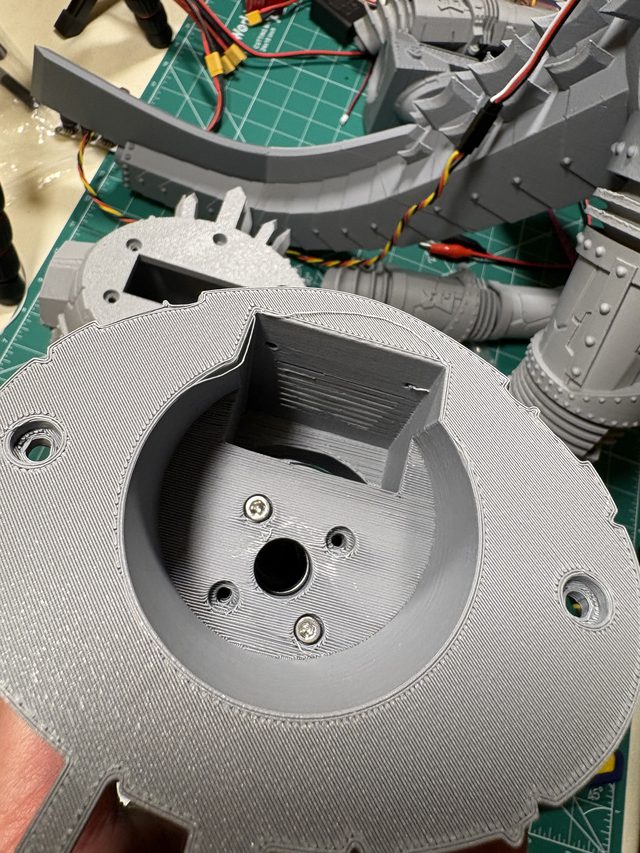 3D-printed base plate with screwed-in servo mount held in hand, tail assembly behind